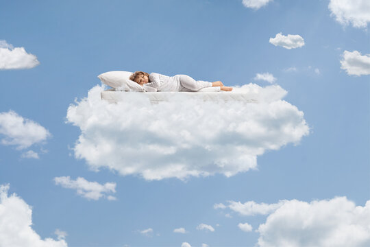 Child in pajamas sleeping over a flying mattress up in the sky