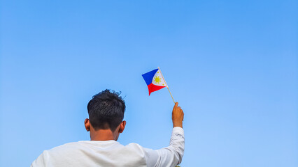 Boy holding Philippines flag against clear blue sky. Man hand waving Filipino flag view from back, copy space