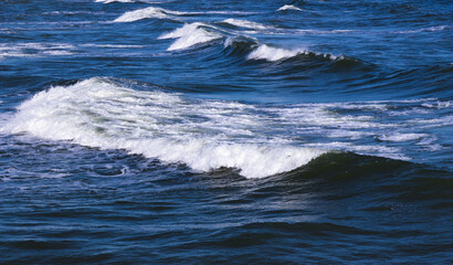 Fototapeta na wymiar Shore waves with white foam goes over deep blue water