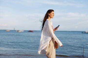 Freelance woman with phone in hand on vacation walking on the beach by the ocean in Bali, happy travel and vacation, mobile communication