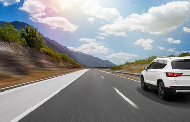 A white car is driving along the road against the backdrop of a mountain landscape.