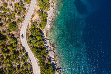 Aerial vertical shot of pickup truck moving by the curved road near sea tranquil waves on coast on...