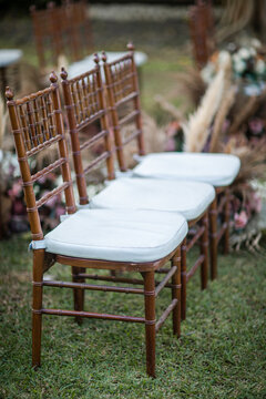 Wedding wooden chairs decorated with flowers. Rustic aisle chairs standing on lawn for ceremony in garden. Natural, shabby, boho wedding decor