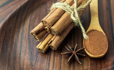 Organic Raw Brown cinnamon sticks Anise star spice fruits and seeds on old wooden table wood stump trunk outdoor walnut plate spoon closeup macro Food Background Vintage Selective Focus.