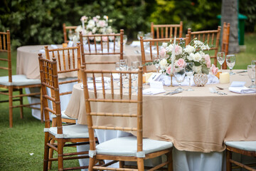 Beautiful outdoor wedding decoration in garden. Round tables decorated with flowers, candles and accessories. Open air wedding banquet on green lawn