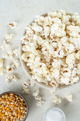 Glass bowl with popcorn, popcorn kernels and salt on a marble table, top view, copy space.