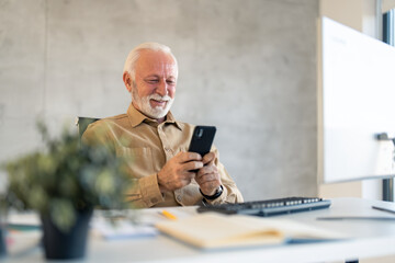 Older senior businessman company worker, professional employee, holding smartphone using cell phone mobile apps reading news, checking financial market data at work in office.