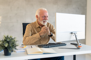Older senior businessman using computer sitting at desk in modern office. Smiling old adult...