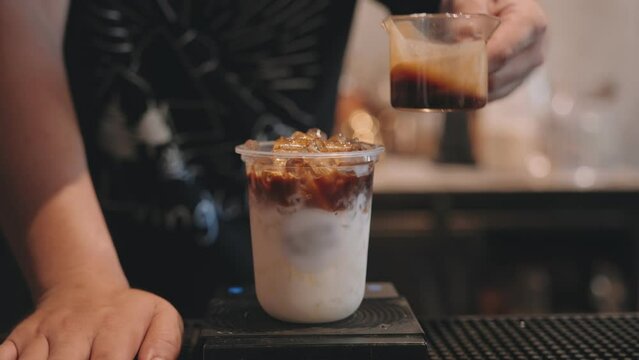 Barista pouring latte coffee with milk in plastic glass on counter at coffee shop