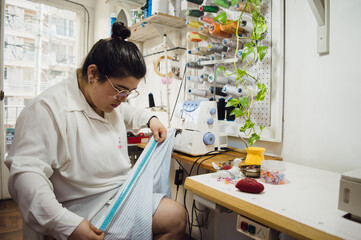 young woman seamstress sitting working measuring fabric with a tape measure