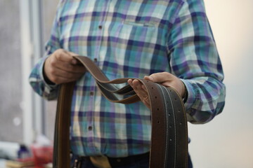 The master holds handmade leather belts with buckles in his hands.