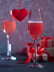 Two glasses of champagne or cider on a side background, gift boxes on Valentine's Day, a red knitted heart. Holiday card