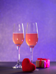 Two glasses of champagne or cider on a side background, gift on Valentine's Day, a red knitted heart. Holiday card