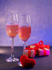 Two glasses of champagne or cider on a side background, gift on Valentine's Day, a red knitted heart. Holiday card