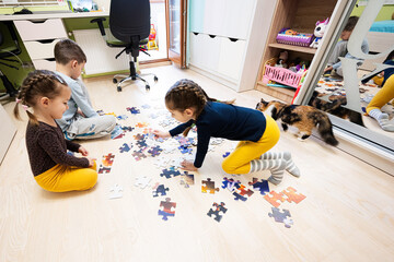 Children connecting jigsaw puzzle pieces in a kids room on floor at home.  Fun family activity leisure.