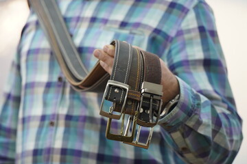The master holds handmade leather belts with buckles in his hands.