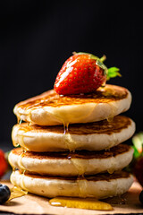 A pile of pancakes with berries and honey. 