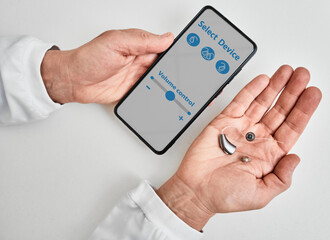 Doctor audiologist showing smartphone app for adjusting hearing aid holding smartphone in one hand...