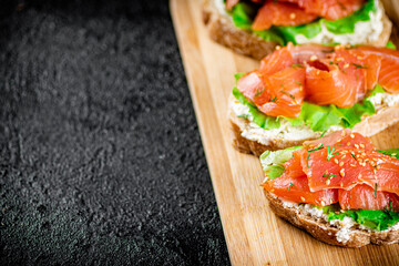 Sandwich with pieces of salmon on a cutting board. 