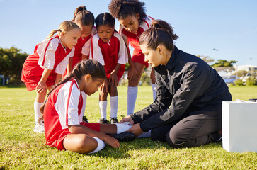 Sports, injury and children soccer team with their coach in a huddle helping a girl athlete. Fitness, training and kid with a sore, pain or muscle sprain after a match on an outdoor football field. - obrazy, fototapety, plakaty