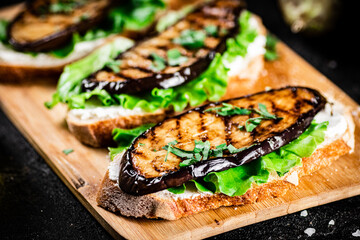 Sandwich with grilled eggplant and lettuce on a wooden cutting board. 