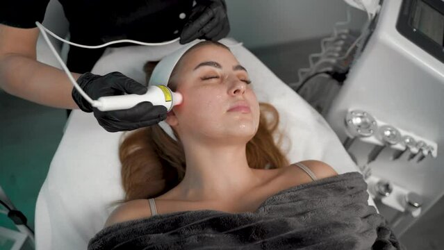 The rf lifting procedure. A woman applies gel to the young lady's face with a brush for the lifting procedure.