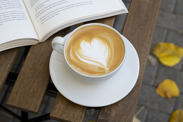 Cappuccino in white cup and book on wooden table