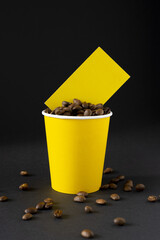 Yellow paper cup of coffee filled with coffee beans with a business card on a black background