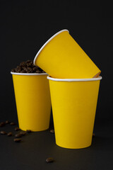 Yellow paper cups of coffee filled with coffee beans on a black background