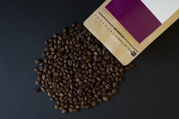 Coffee bag with open beans around on black background
