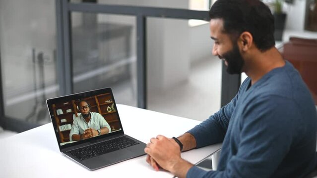 Two diverse male colleagues taking part in video meeting. Multiracial business partners involved virtual conference. Back view male Indian student takes an online language classes from African teacher