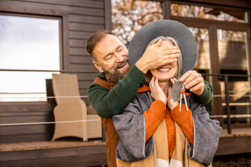 Man closing eyes to his wife and holding keys from new home