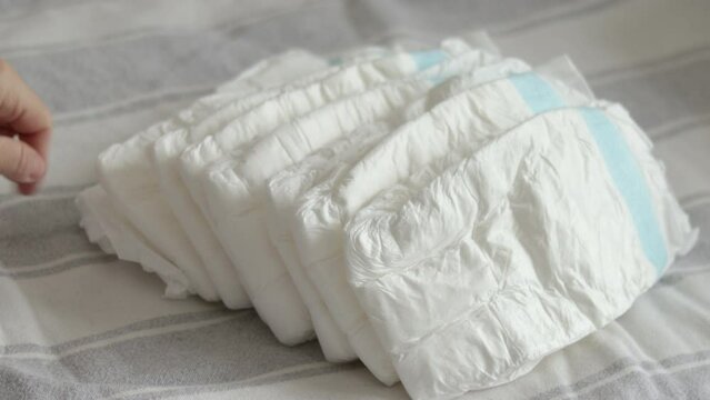 baby diapers in pack woman mother hand or bed finger counting throwing on blanket chaotic or in row arrangment.mom hand hold new diaper white no paint drawn close up 4k slow motion motherhood 