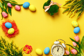 Easter frame. Eggs bunny flowers alarm clock on a yellow background. Place for text