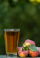 Apple juice in a glass with fresh ripe apples on a wooden table in the garden, around it are apples trees. Tasting fresh juice in the orchard in a summer day outdoors close-up
