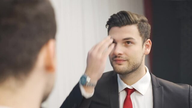 Businessman applying gel to his hair in front of the mirror.
Young businessman applying gel to his hair to look cool and good.
