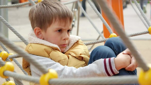Upset and sad little boy being victim of bullying sitting alone on school playground. Child depression, problems with bullying, victim in school, emigration, criminal and poverty.
