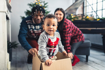 Toddler boy with multiracial parents playing with a cardboard box . High quality photo