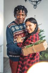 Obraz premium Interacial couple standing together with presents near the Christmas tree. High quality photo