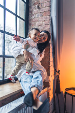 Vertical shot of a happy woman with her toddler son on a window sill. High quality photo