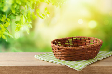Fototapeta na wymiar Empty basket with tablecloth on wooden table over green garden background. Spring or Easter mock up for design and product display.