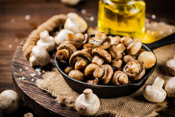 Frying pan with fried mushrooms on a wooden tray. 
