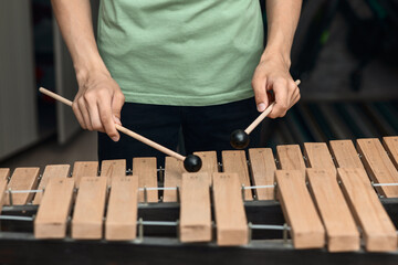 Hands of a young musician playing sticks on a wooden musical instrument xylophone, close-up, selective focus - obrazy, fototapety, plakaty