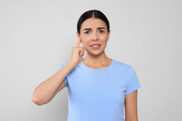 Young woman suffering from ear pain on light grey background