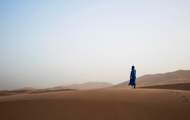 Fototapeta na wymiar Woman standing on a large sand dune in the sahara. Merzouga desert. Morocco. One person standing alone in the desert looking towards the dunes. 