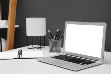Comfortable workplace at home. Modern laptop with blank screen and stationery on white wooden desk. Mockup for design