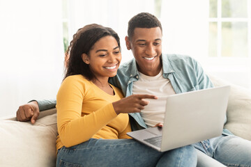 Fototapeta premium Smiling young african american man and woman point finger at laptop, have video call, chat online