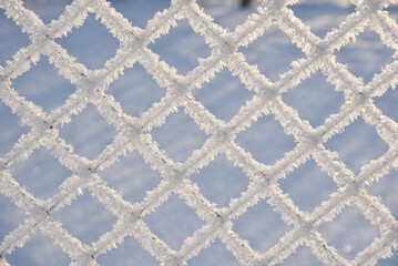 Snow frost on the iron fence of the fence. Mesh netting. Snow patterns on iron.
