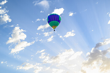 Colorful hot air balloon flying over blue sky with white clouds