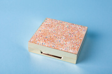 Closed Eyeshadow palette for make-up on blue background. Classic Eyeshadow palette with facial mirror. Closed metallic box with shining rhinestones on the top.